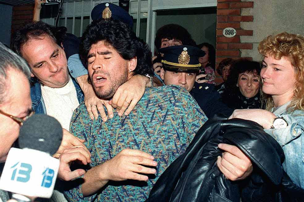 En Nápoles Maradona llegó a la cumbre de su juego… y de su desenfreno. En una ciudad en la que la droga corría a raudales, Diego consumía cocaína con regularidad, según contó él, durante fiestas que comenzaban tras el partido del domingo y se prolongaban hasta el miércoles, en que empezaba a ‘desintoxicarse’ y entrenaba otros tres días de manera desmedida. Solo un portento físico podía aguantar aquello. Pero no podía durar. Su relación con una familia de mafiosos y los escándalos acabaron el 26 de abril de 1991 con su detención en Argentina (en la imagen) por posesión de drogas. No llegó a ir a la cárcel, pero fue el principio de su caída.